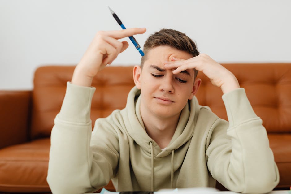 A stressed teenager in a hoodie struggles with homework, deep in thought indoors.